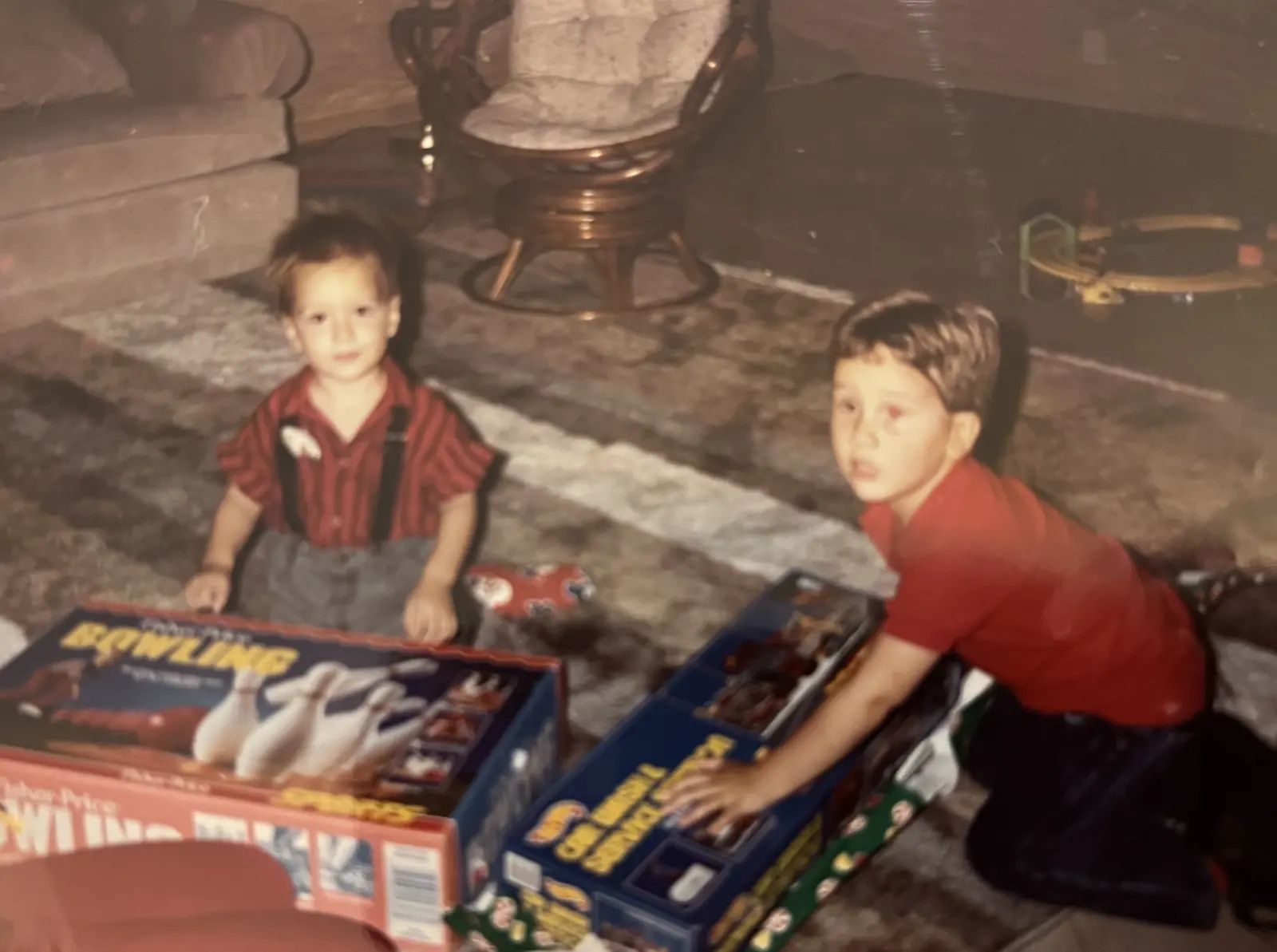 Two boys on a living room floor on Christmas morning, a Fisher-Price bowling set and a Hot Wheels service station still in their boxes